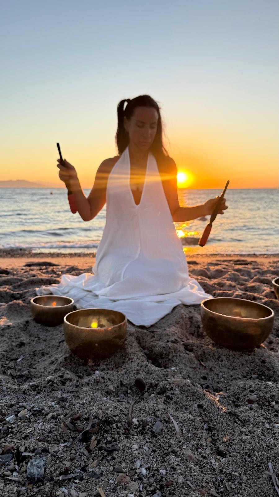 Gem playing Tibetan singing bowls with strikers at sunset
