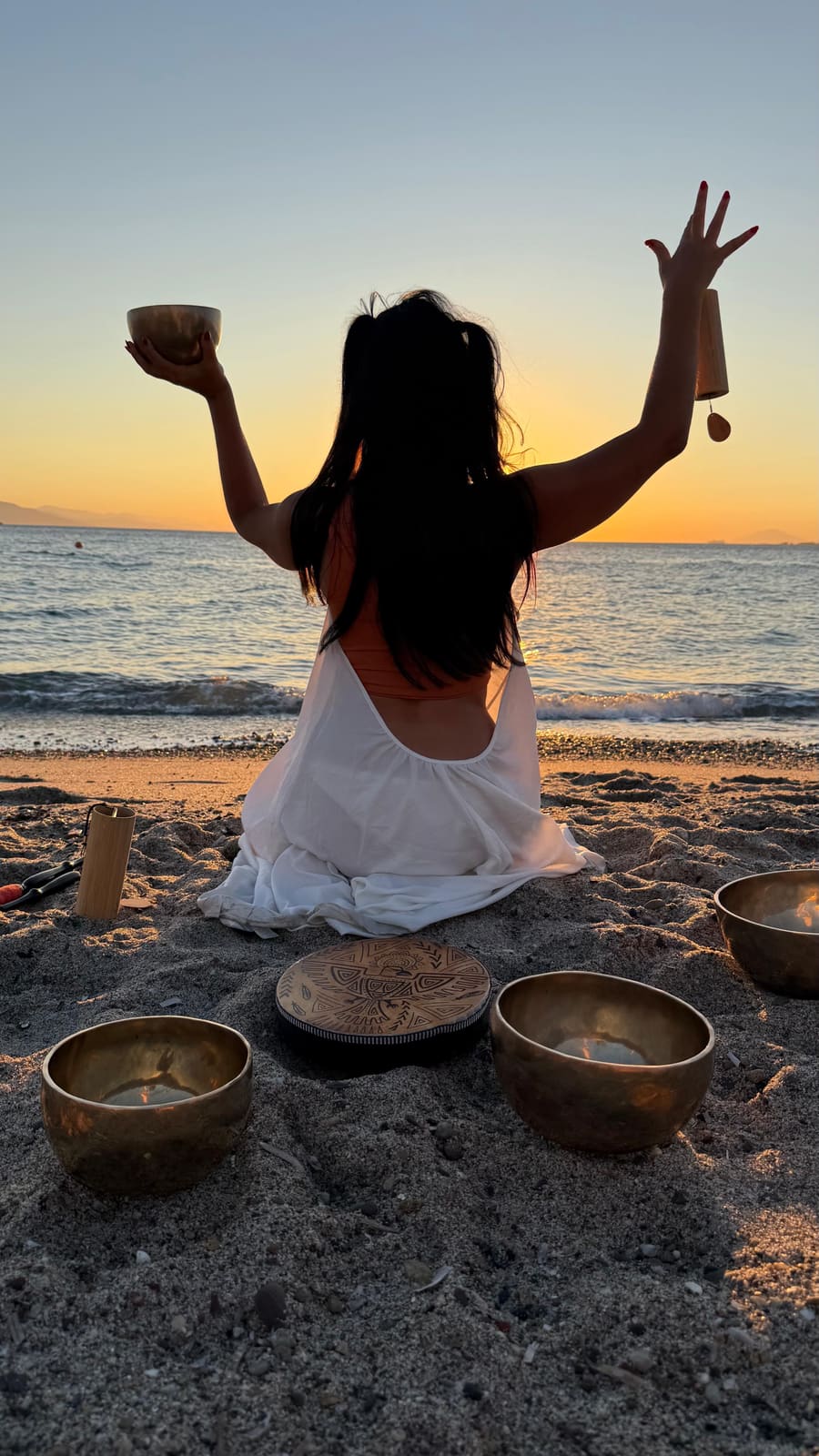 Gem playing chimes over singing bowls on the shoreline at sunset