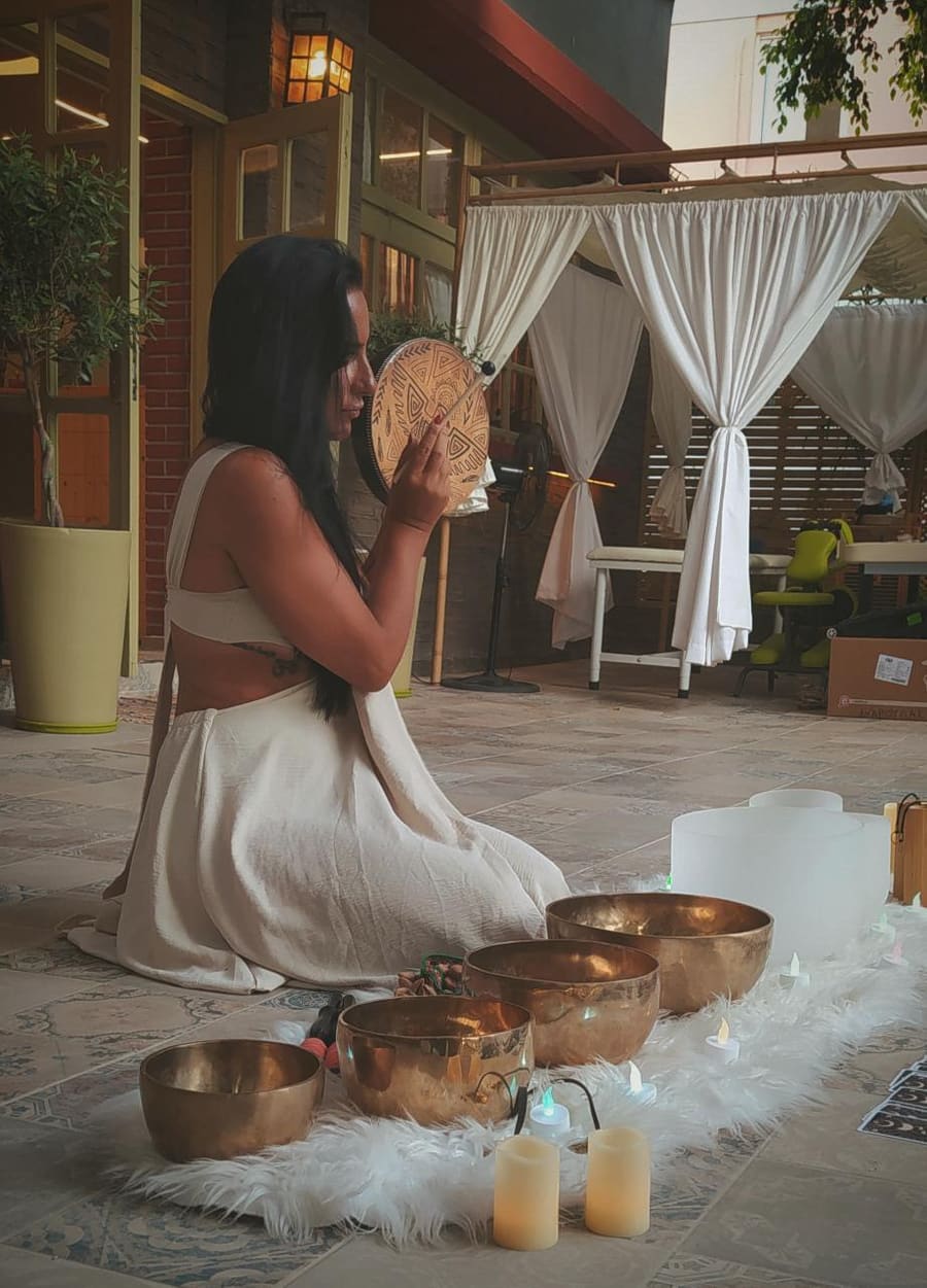Gem playing a frame drum beside singing bowls at a wellness venue
