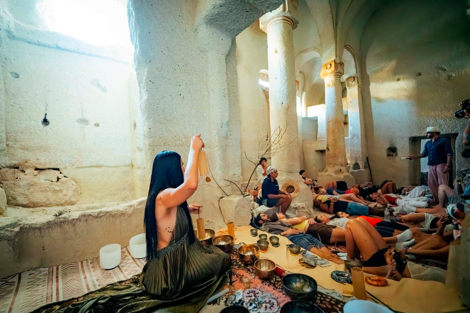 Gem raising a chime over a room of resting participants during a sound journey in a rock-hewn chapel