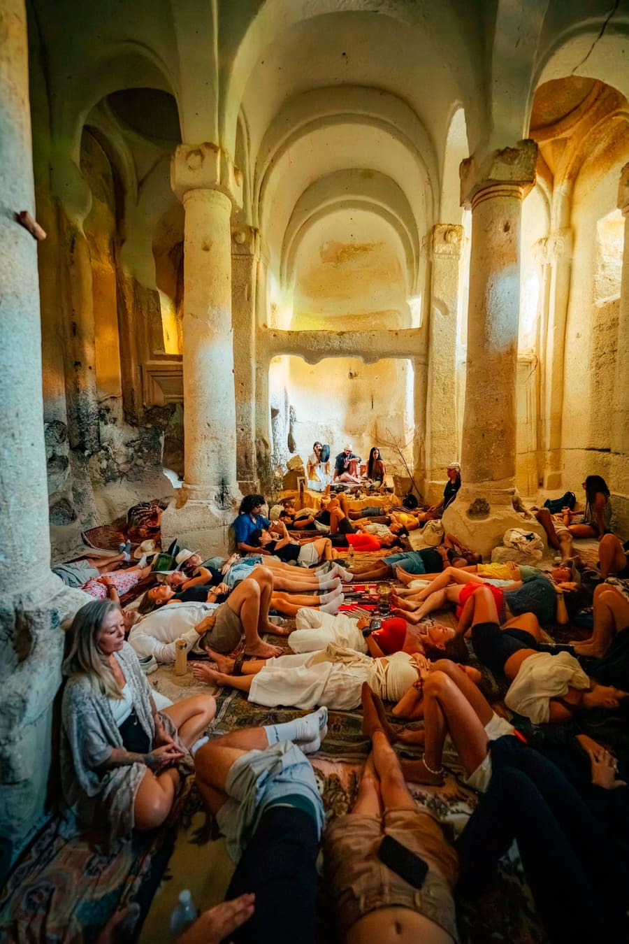 Retreat guests resting on mats during a sound ceremony in a columned rock chapel